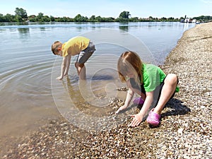 A boy and a girl are playing on the beach. Children play with water, sand and pebbles on the river bank.