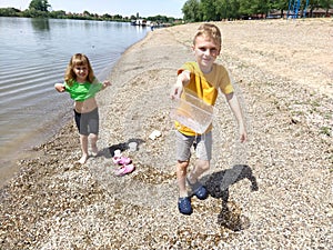 A boy and a girl are playing on the beach. Children play with water, sand and pebbles on the river bank. Kids are dressed in plain