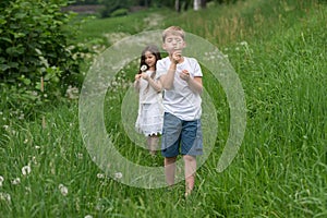 A boy with a girl playing in a field with dandelions.