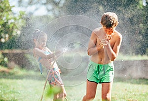 Boy and girl playing in garden, pouring with water each other from the hose, making a rain. Happy childhood concept image