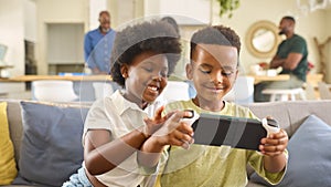Boy And Girl  Playing With Handheld Gaming Device At Home With Multi Generation Family In Background photo