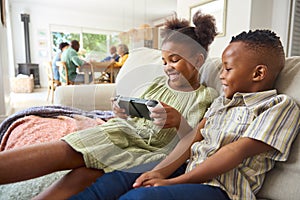 Boy And Girl Playing With Handheld Gaming Device At Home With Multi-Generation Family In Background photo