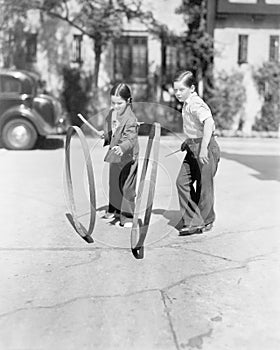 Boy and girl playing hoop and stick on a sidewalk