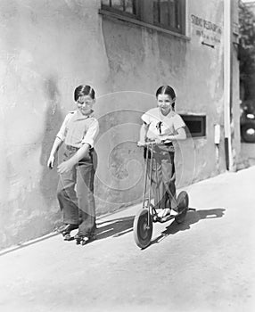 Boy and girl playing on a scooter and the other on roller blades