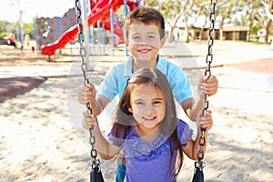 Boy And Girl Playing On Swing In Park