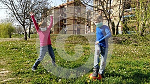 A boy and a girl in protective surgical masks play a ball and dance on the green grass. Protection against airborne diseases. The