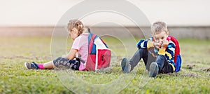 A boy and a girl quarreling and are sitting on the grass in the schoolyard back to back