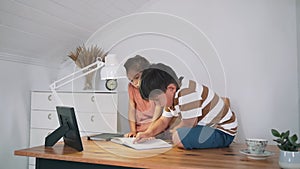 A boy and a girl are reading a book sitting on a table. The children are doing their homework. Home education