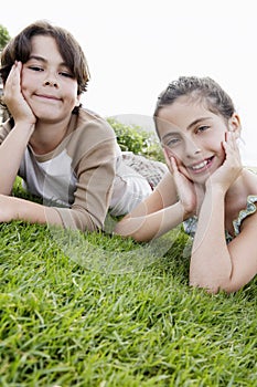 Boy And Girl Resting Chin In Hands While Lying On Grass