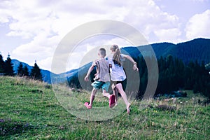 A boy and a girl are running on the grass. Outdoors. On the background of mountains