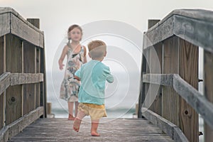 Boy and girl running on wooden boardwalk on the beach