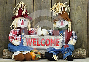 Boy and girl scarecrows sitting on log holding red wood welcome sign