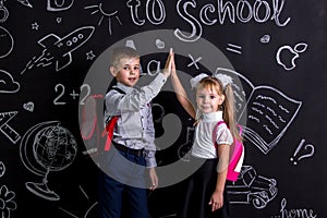 Boy and girl. School mates standing before the chalkboard as a background with a backpack on their backs claping their