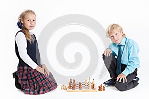 Boy and girl in school uniform playing chess, looking at camera, isolated white background