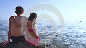 Boy and girl on the sea. A boy and a girl are sitting on the rocks on the sea view from the back of a romance happy