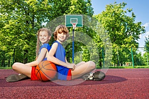 Boy and girl sit with backs close on playground