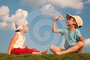 Boy and girl sit on grass and drink from bottle