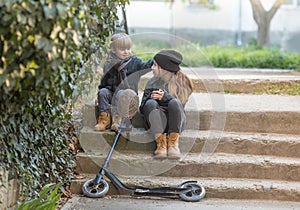 A boy and a girl sit on the steps with a scooter.