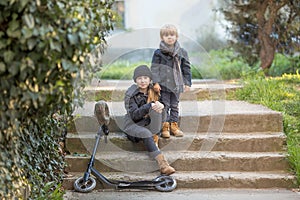 A boy and a girl sit on the steps with a scooter.