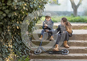 A boy and a girl sit on the steps with a scooter.