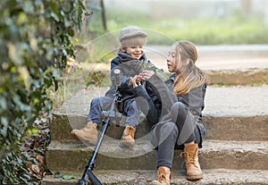 A boy and a girl sit on the steps with a scooter.