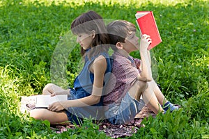 Boy and girl are sitting back-to-back on the lawn in the park and reading books.