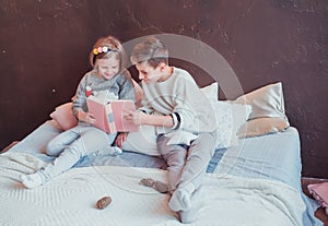 Boy and girl sitting on the bed and reading a book. Cozy interior in warm colors