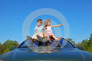 Boy and girl sitting on car roof on sky