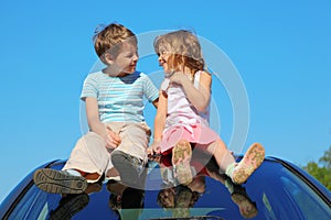 Boy and girl sitting on car roof on sky