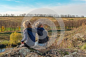 A boy and a girl are sitting on a cliff, two friends, a brother and a sister, are hugging each other.