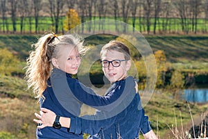 A boy with a girl are sitting on a cliff, two friends, a brother and sister are sitting in an embrace and look into the camera thr