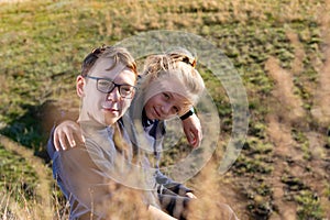 A boy with a girl are sitting on a cliff, two friends, a brother and sister are sitting in an embrace and look into the camera thr