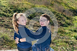 A boy with a girl are sitting on a cliff, two friends, a brother and sister are sitting in an embrace and look into the camera thr