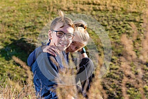 A boy with a girl are sitting on a cliff, two friends, a brother and sister are sitting in an embrace and look into the camera thr