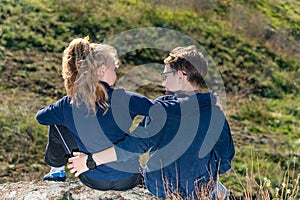 A boy with a girl are sitting on a cliff, two friends, a brother and sister are sitting in an embrace and look at each other.