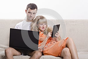 A boy and a girl sitting on the couch with the laptop and tablet