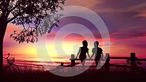 A boy and a girl sitting on the fence against bright sea sunset