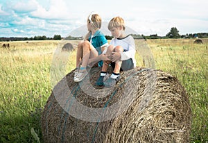 Boy with a girl sitting on haystack the background of summer meadows