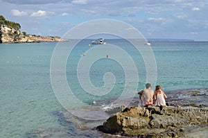 Boy and Girl Sitting on a Rock of Cala Major Beach in Palma de Mallorca, Spain