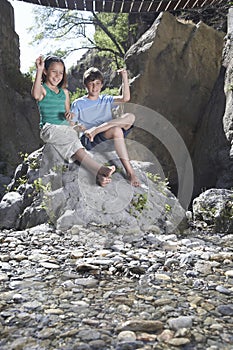Boy and girl (10-12) sitting on rock throwing stones
