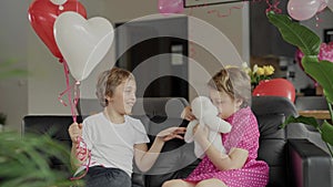 Boy and girl are sitting in the sofa in the decorated room for Valentine's Day.
