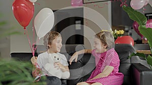 Boy and girl are sitting in the sofa in the decorated room for Valentine's Day.