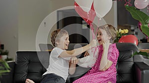 Boy and girl are sitting in the sofa in the decorated room for Valentine's Day.