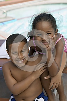 Boy (7-9) and girl (5-6) sitting by swimming pool portrait.