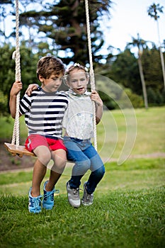 Boy and girl sitting on a swing in park