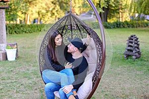 Boy and girl sitting together in suspended chair, hugging each o