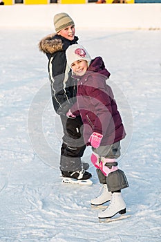 Boy and girl skating on rink hand in hand in winter