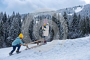 Boy and girl sledding in a snowy forest. Outdoor winter kids fun for Christmas and New Year. Children enjoying a sleigh