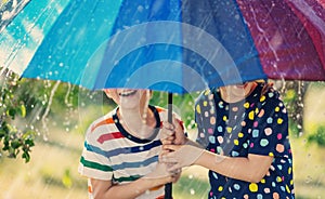 Boy and girl standing outdoors in rainy day under colourful umbrella.