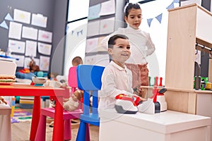 Boy and girl students playing supermarket game sitting on table at kindergarten